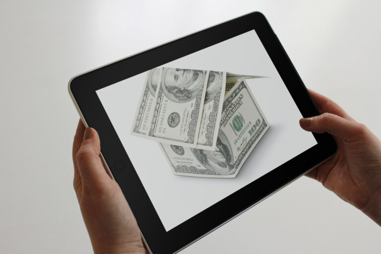 A woman holding an iPad with an image of a house made of money.